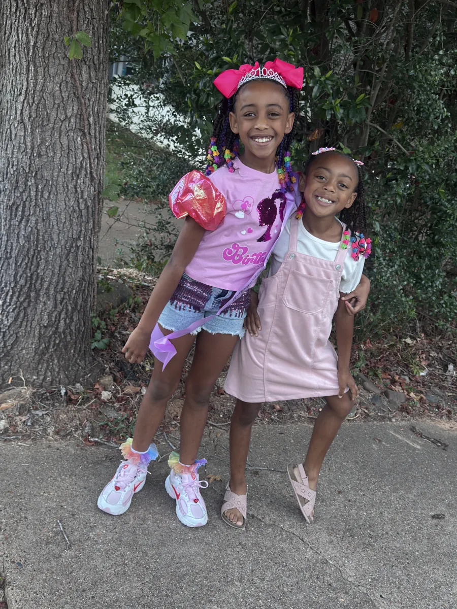 The sisters hugging on a birthday, one wearing a tiara and big pink bow